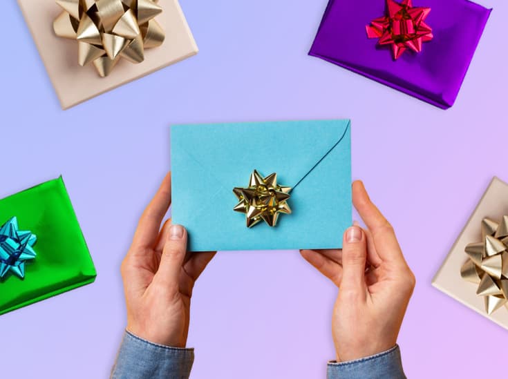 Twee handen houden een blauwe envelop met gouden strik vast, omringd door ingepakte cadeaus