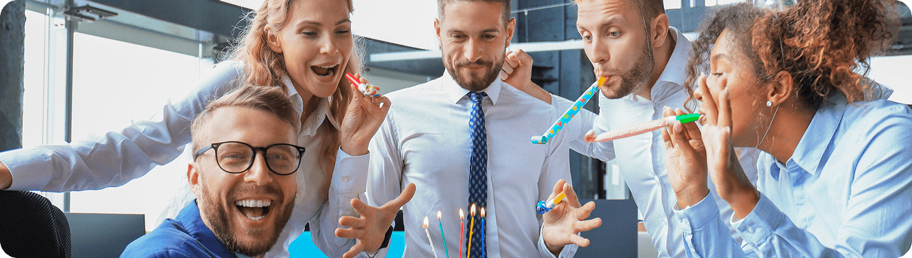 Een groep collega's viert uitbundig met toeters rond een taart met kaarsjes