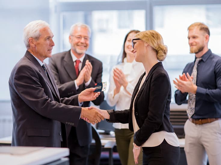 Manager overhandigt een medewerker een cadeaukaart terwijl het team applaudisseert
